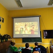 Students are watching a film projected on a screen in the classroom