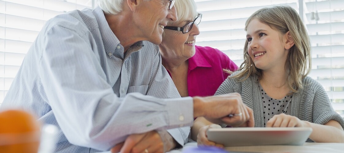 grandfather, grandmother and granddaughter are sitting at the tablet