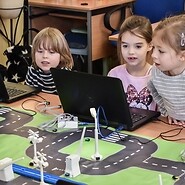 Trójka dzieci wpatrzona w ekran laptopa przed makietą Inteligentnego Miasta