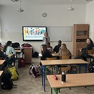 Klasa szkolna z uczniami siedzącymi przy ławkach, patrząc na ekran z prezentacją.