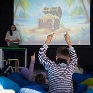 dzieci siedzą na podłodze patrzą się na ekran z prezentacją