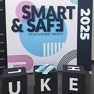 duży roll up z napisem Smart&amp;Safe przed plakatem stoją trzy czarne ...