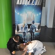 dzieci podczas nauki kodowania, w tle roll up z grafiką koduj z UKE