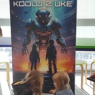 dzieci podczas nauki kodowania, w tle roll up z grafiką koduj z UKE
