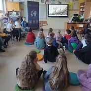 dzieci siedzą na podłodze i słuchają wykładu