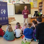 dzieci siedzą na podłodze i słuchają wykładu