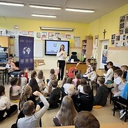 dzieci siedzą na podłodze i słuchają wykładu