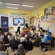 dzieci siedzą na podłodze i słuchają wykładu